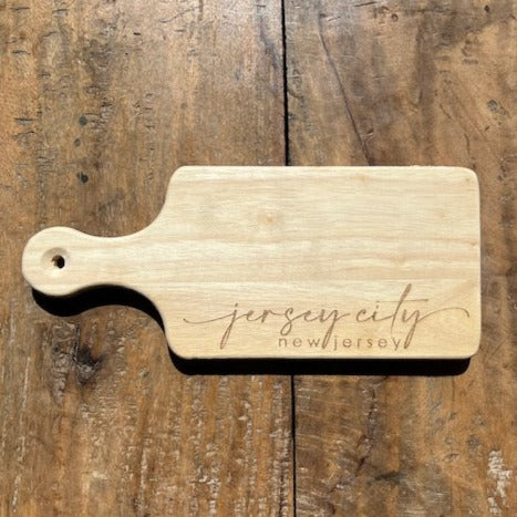 Rectangular cutting board with a handle that reads "Jersey City, New Jersey" 