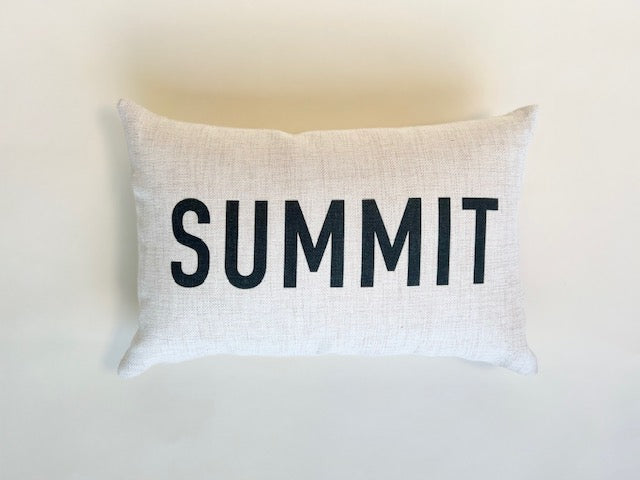 Small rectangular cream pillow that reads Summit in black letters