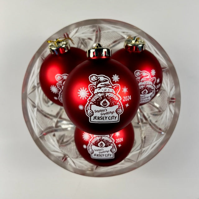 Red Christmas ornament with a racoon on it holding a sign that says "Season's Greetings Jersey City 2024" 