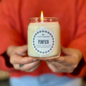 A person holding a lit Pumpkin scented soy & beeswax candle in a glass car. 