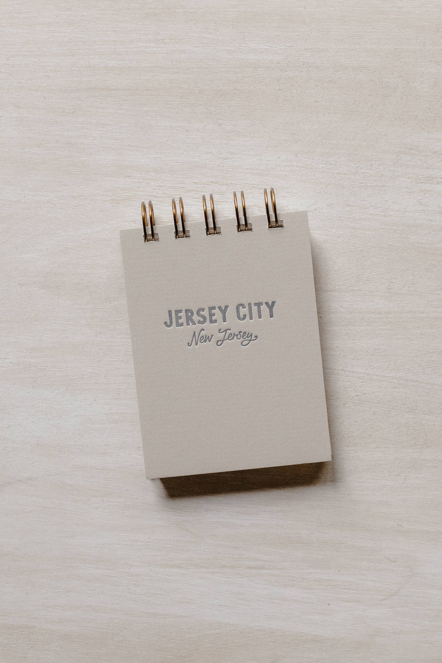 A tan rectangular mini jotter notepad that reads "Jersey City, NJ" on the cover